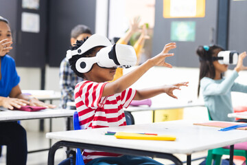 In school, diverse students wearing virtual reality headsets are reaching out in the classroom