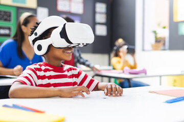 In school, young African American boy wearing a VR headset sits at a desk in the classroom, copy spa - Powered by Adobe