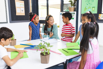 In school, middle-aged Asian woman teaching sustainability to diverse children in classroom