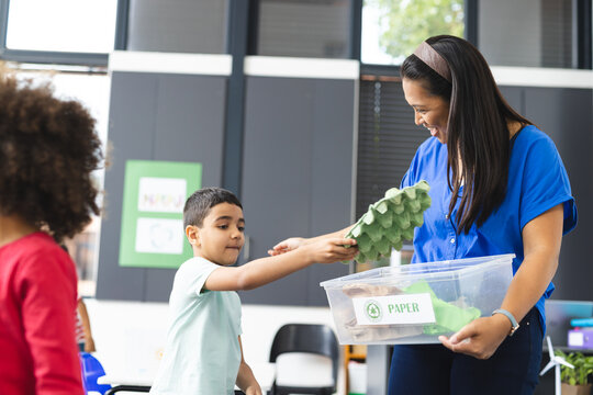 In school, in the classroom, a diverse teacher is showing recycling to two young students
