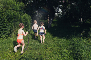 Two children run away from a girl with a hose. Children boy and girls in a swimsuit plays with...