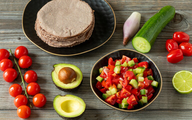 Pico de Gallo salsa, red corn tortillas, avocado, lime, cucumber, and tomatoes. Rustic wooden table. Healthy vegan Mexican food.