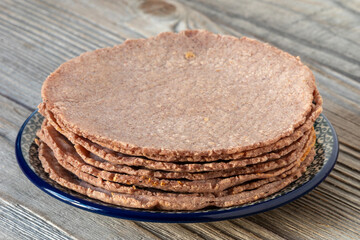 Close-up view of a stack of homemade red corn tortillas on a black plate. Rustic wooden table. Healthy vegan Mexican food.