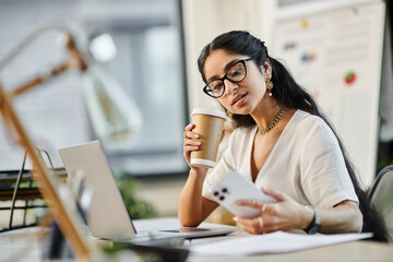 Young indian woman engaged in work at desk with laptop and coffee.