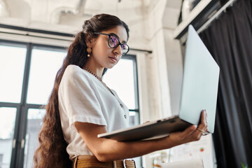 Attractive indian woman with glasses using laptop in office.