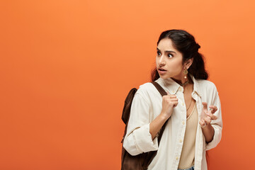 Young indian woman with backpack against orange wall