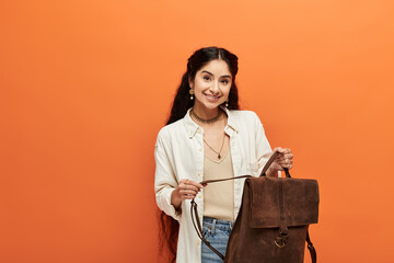Young indian woman holding backpack against vibrant orange background.