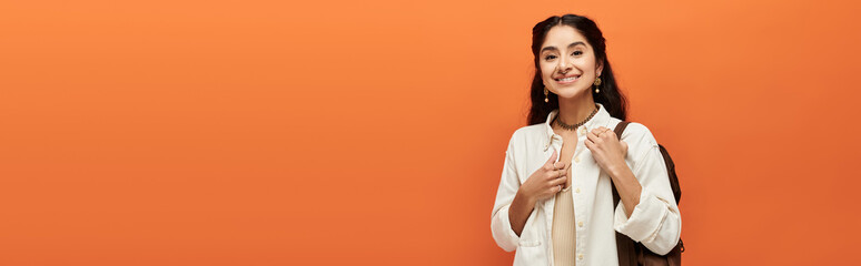 A indian woman beams with joy on a vibrant orange backdrop.