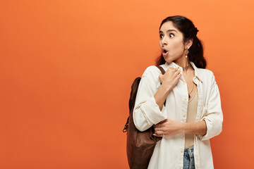 Young indian woman with backpack stands against vivid orange background.