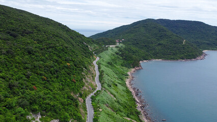 Aerial view of countryside road passing through the green forest and mountain