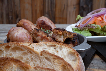 Traditional asado criollo plate. Closeup view of chorizos, pork sausages, grilled sweetbreads, potatoes, bread, and a traditional salad with lettuce, tomato and onion.