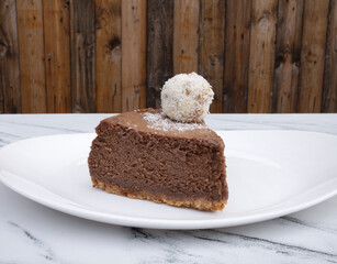 Sweet dessert. Closeup of a slice of chocolate cheesecake with a coconut truffle, in a white plate.	
