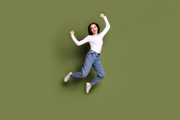 Full body photo of attractive young woman jump winning raise fists dressed stylish white clothes isolated on khaki color background