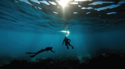 Silhouette of two scuba divers exploring under the ocean with sunbeams filtering through