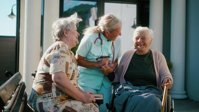Female nurse and two pensioners are talking and socializing out in the courtyard of a nursing home