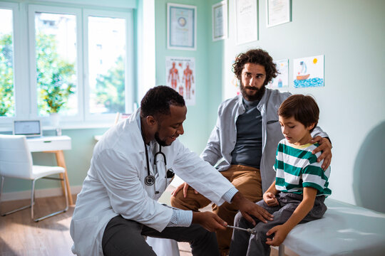 Pediatrician checking reflexes of a young boy in a medical clinic with his father present