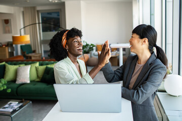 Two professional women celebrating success with a high-five in a stylish office