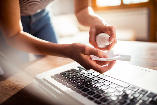 Woman disinfecting laptop keyboard with cleaning wipe