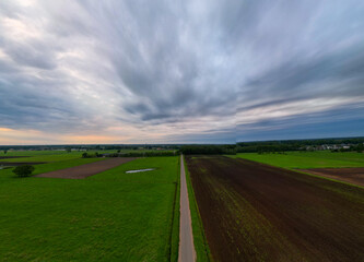A serene countryside scene unfolds with a quiet road winding through lush landscape under dramatic cloudy skies