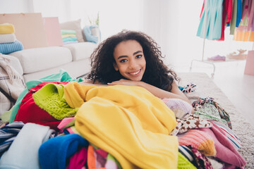 Photo of pretty young woman toothy smile lying messy pile stack clothes apartment indoors