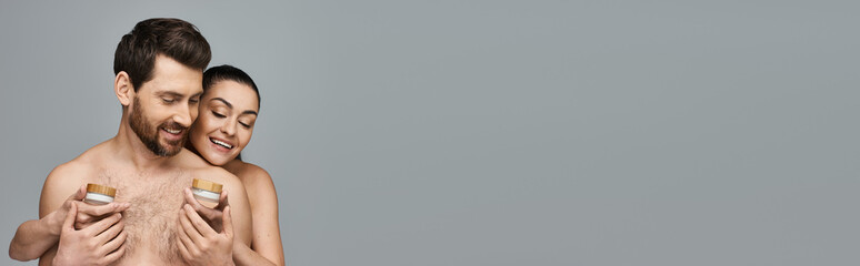 Handsome man and beautiful woman holding skincare products tenderly.