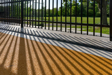 Late afternoon image of an ornamental metal trench drain in concrete with shadow pattern from an adjacent ornamental fence.