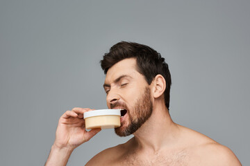Bearded man biting a jar of cream.