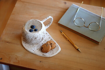 Cup of blueberry and banana smoothie, chocolate chip cookies, book, pen and reading glasses on the...