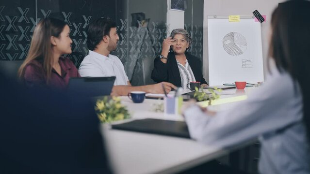 Indian Asian happy older female old elder lady boss young adult girls boy male expert staff group team man agent sitting chair talk share project profit plan good news new ideas office job work place