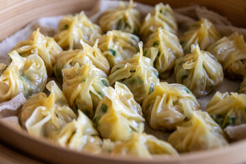 Steamed dumplings - vibrant green herbs and succulent meat visible - nestled in a bamboo steamer with a glossy appearance. Taken in Toronto, Canada.