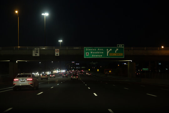Nighttime highway with vehicles in motion illuminated by streetlights - directional signs for Steeles Ave and Woodbine Avenue. Taken in Toronto, Canada.