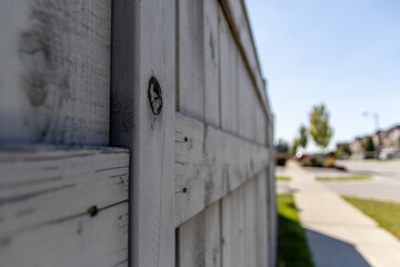 Close-up view of weathered wooden fence - suburban neighborhood backdrop - knot in wood and peeling white paint - clear blue sky. Taken in Toronto, Canada.