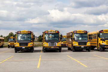 Yellow school buses lined up in an empty parking lot - under a partly cloudy sky. Taken in Toronto, Canada.