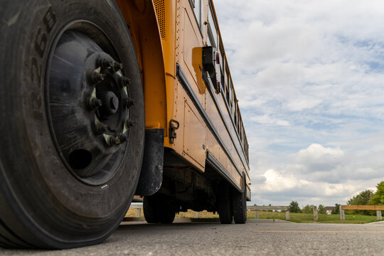 Low angle view of yellow school bus - detailed tire and body - cloudy sky backdrop. Taken in Toronto, Canada.