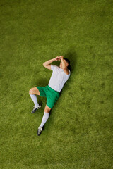 Bird's eye view of footballer on ground, covering his face with both hands, expressing emotions of...