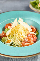 Caesar salad with smoked salmon, cheese, and boiled eggs on a turquoise plate