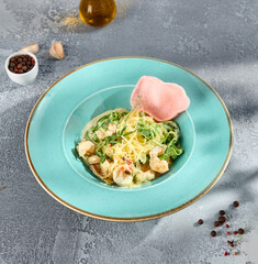 Shrimp pasta elegantly plated on a turquoise dish, garnished with a crisp pink tuile and...