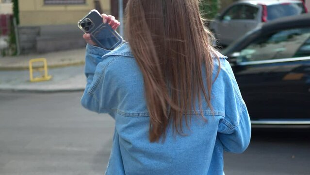 Woman crossing road outdoors, back view. Camera moving after her