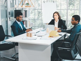 Businesspeople's multiracial colleagues brainstorm with house models and blueprints at the office. Professional construction team discussing the arrangement of service lines at the new building..