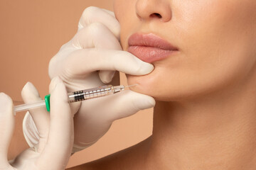 Close up of young woman getting collagen injection in her chin, having beauty treatment, beige...