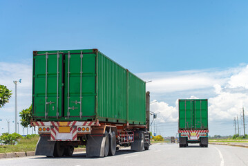 Two green container trucks driving on a highway under a clear blue sky, emphasizing transportation...