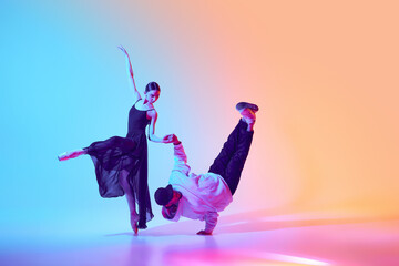 Classical ballerina and a contemporary street dancer making breathtaking creative performance, dancing against gradient background in neon light. Concept of classical and modern dance, performance
