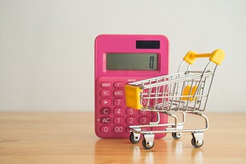 Calculator and shopping cart trolley on wooden table with white wall background copy space. Home...