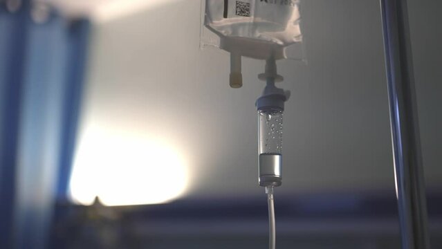 Close-up of hospital IV drip attached to metal stand in hospital room with a saline plastic bag hanging.