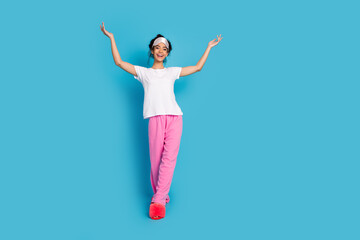 Full size photo of nice young woman raise arms walk empty space wear pajama isolated on blue color background