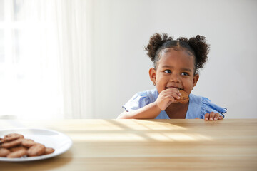 African child girl picking and eating chocolate cookies or biscuits from dish