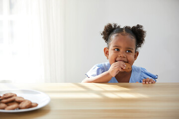 Fototapeta premium African child girl picking and eating chocolate cookies or biscuits from dish