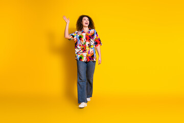 Full length photo of lovely young lady walk wave arm empty space dressed stylish colorful print garment isolated on yellow color background