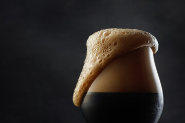 Dark beer with overflowing foam head. Selective focus. Copy space