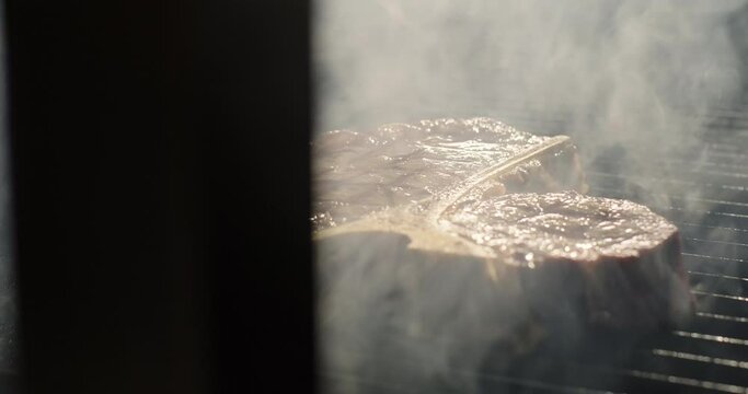 T-bone steak on BBQ grid in smoke. Grilling BBQ meat. Close-up